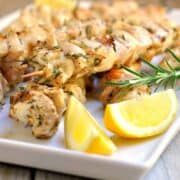 Rosemary garlic chicken kabobs on a white serving tray with fresh lemon.