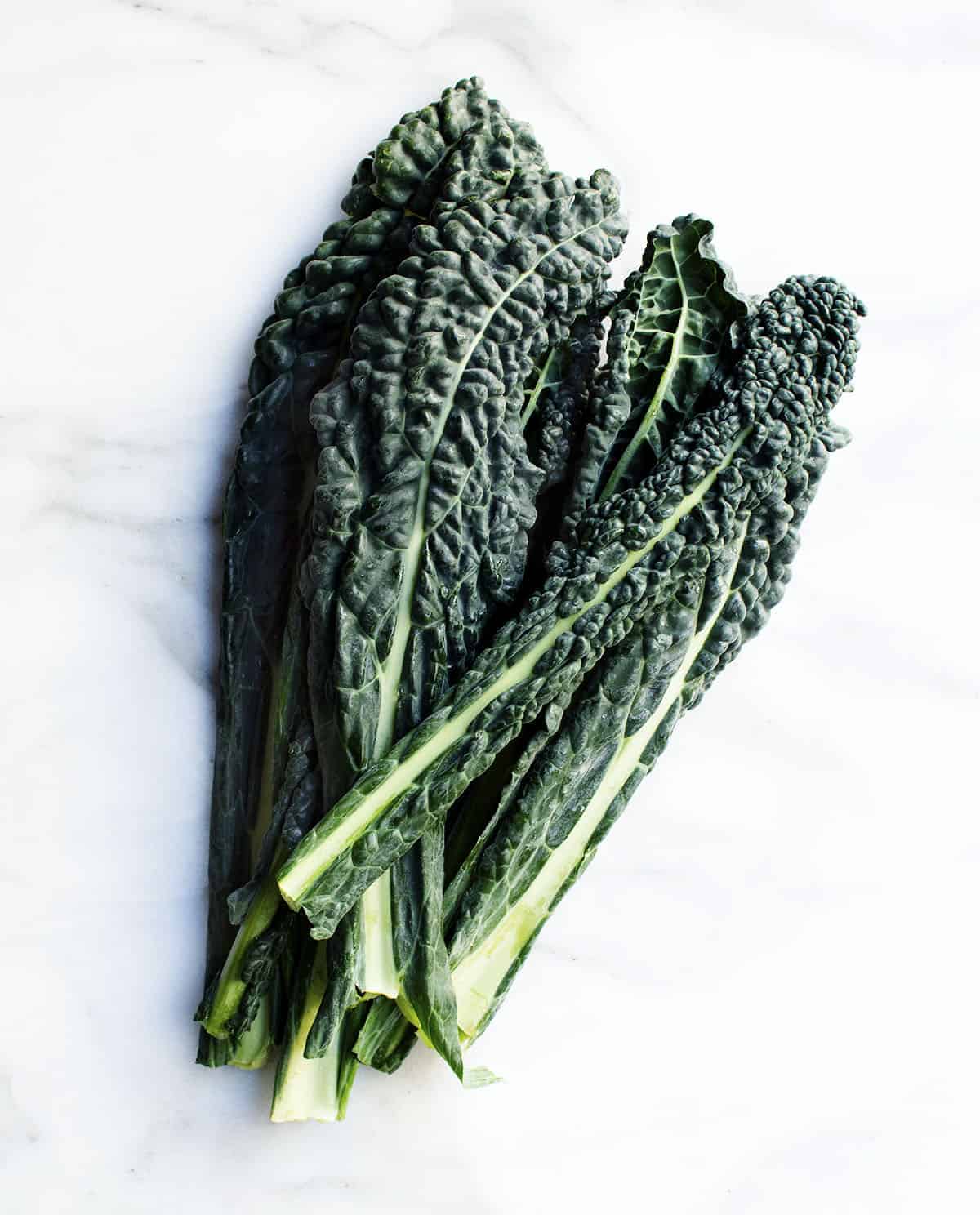 a bunch of lacinato kale on a white marble board