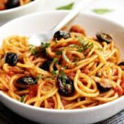 spaghetti alla puttanesca served in a white bowl with a black napkin underneath