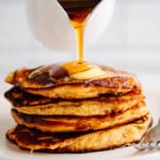 pouring maple syrup over a stack of Almond Flour Banana Pancakes