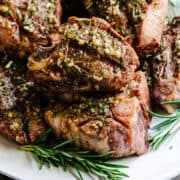 Grilled Lamb Loin Chops stacked on a white platter with rosemary sprigs.