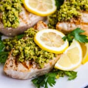 Grilled Swordfish served on a platter and topped with green olive tapenade, lemon slices and parsley.
