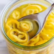 Spooning pickled banana peppers out of a glass jar.