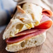 Brown paper parchment wrapped Jambon Beurre sandwich on a wooden board.