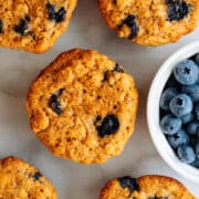 Banana Blueberry Oatmeal Muffins on a white marble board with a bowl of fresh blueberries.