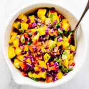mango salsa served in a white ceramic bowl with a serving spoon.