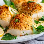 parmesan baked cod served with parsley and lemon slices on a white oval platter.