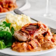 Pork Saltimbocca served on a white plate with greens and mashed potatoes.
