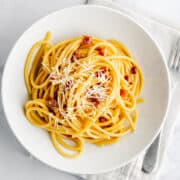 Bucatini Carbonara served in a white bowl on a linen napkin.