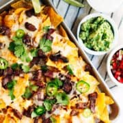 Carne Asada Nachos served in a rimmed baking sheet with guacamole salsa and sour cream.