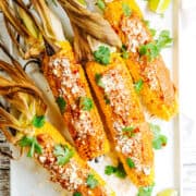 Mexican Corn on the Cob served on a white rectangular platter with lime wedges photographed from above.