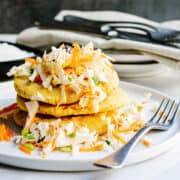 Pupusas stacked on a white plate with curtido.