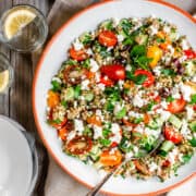 Tabouli Salad served in a white shallow bowl with glasses of water and lemon slices photographed from above.
