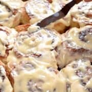 spreading cream cheese frosting on warm cinnamon rolls