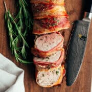 Bacon Wrapped Pork Tenderloin sliced and served on a wooden board and photographed from overhead.
