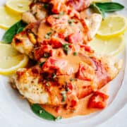 Chicken Saltimbocca served with lemon slices and sage leaves on a white oval platter.