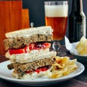 Meatloaf Sandwich served on a plate with potato chips and a beer in the background.