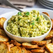 Artichoke Tapenade served in a white bowl surrounded by round toasts.