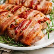 Bacon Wrapped Pork Chops served on a white oval platter with rosemary sprigs.