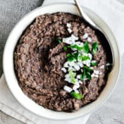 Refried Black Beans in a white bowl with a stainless steel serving spoon.