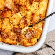 Brioche French Toast Casserole in a white ceramic baking dish with a serving spoon photographed from overhead.
