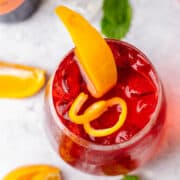 Campari Spritz cocktail photographed from the top on a white surface with orange slices and ice cubes.