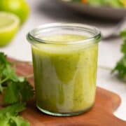 Cilantro Lime Vinaigrette in a clear glass container on a wooden board.