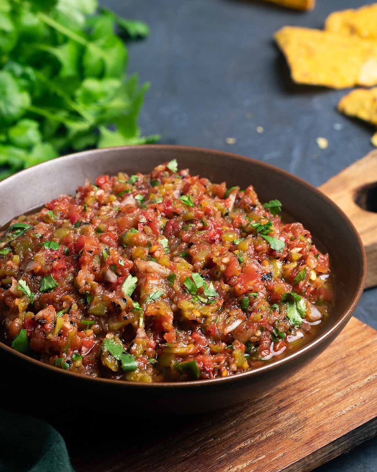 Fire Roasted Salsa served in a brown ceramic bowl on a wooden board and photographed from an angle.
