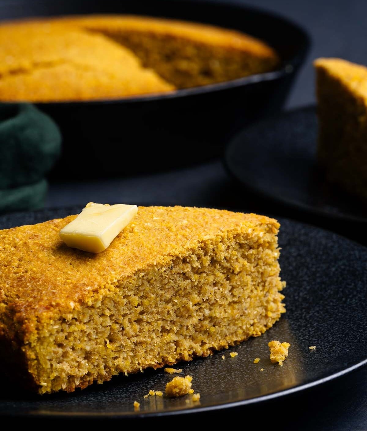 A slice of Sweet Potato Cornbread on a black plate with a pat of butter.