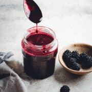 Blackberry Syrup dripping off a spoon into a glass jar.