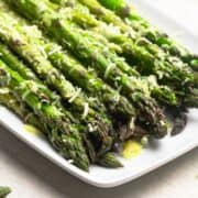 Garlic Parmesan Asparagus served on a white rectangular platter and photographed close up from an angle.