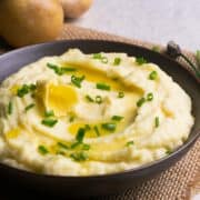 Sour Cream Mashed Potatoes served in a black bowl with butter and photographed at an angle.