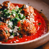 Five Lamb Meatballs served in red sauce and photographed at an angle.