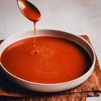 Homemade Red Enchilada Sauce dripping from a spoon over a bowl.