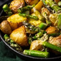 Roasted Potatoes and Asparagus photographed at an angle in a black bowl.