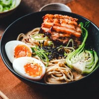 A bowl of miso ramen with noodles, two soft-boiled egg halves, sliced grilled pork, green onions, seaweed, and bok choy in broth, garnished with sesame seeds, on a wooden table.