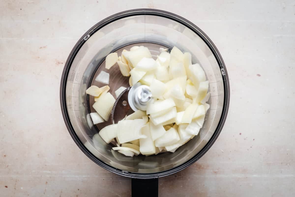 Chopped onions in a food processor bowl on a light countertop.
