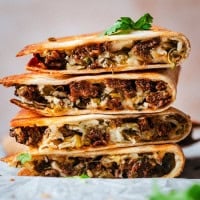 A stack of crispy, golden chorizo quesadilla wedges filled with melted cheese, seasoned meat, and herbs, garnished with fresh cilantro.