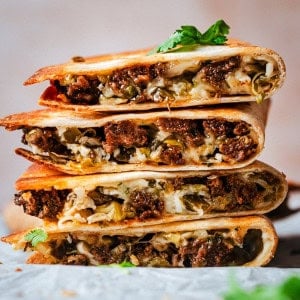 A stack of crispy, golden chorizo quesadilla wedges filled with melted cheese, seasoned meat, and herbs, garnished with fresh cilantro.