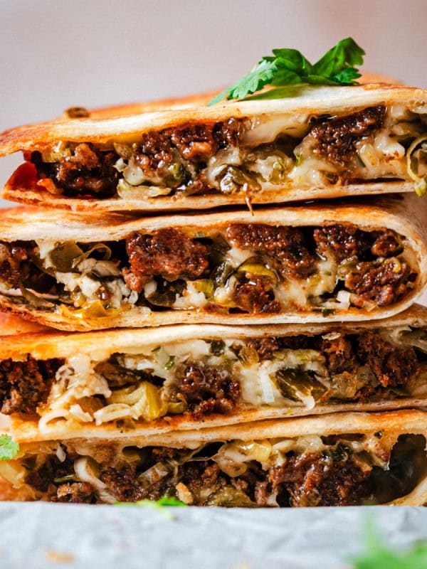 A stack of crispy, golden chorizo quesadilla wedges filled with melted cheese, seasoned meat, and herbs, garnished with fresh cilantro.
