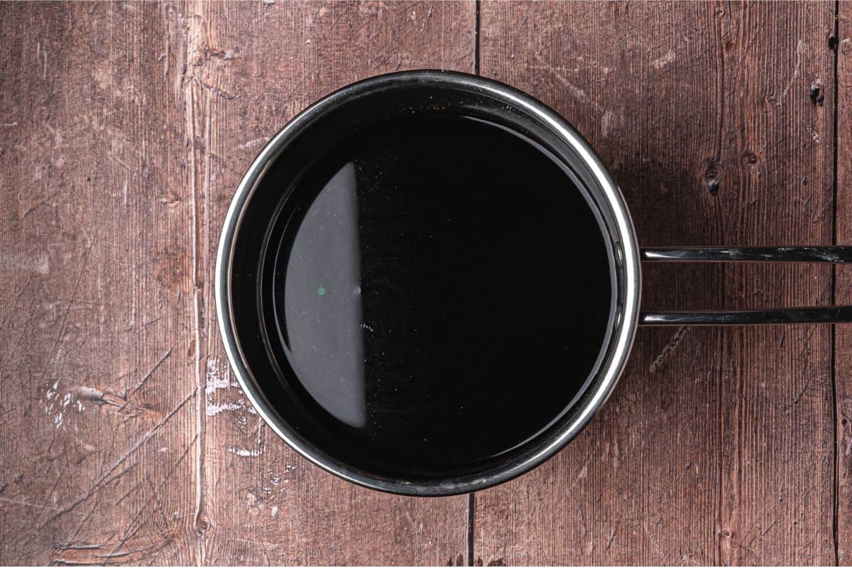 A metal saucepan filled with a dark liquid sits on a rustic wooden surface, viewed from above.