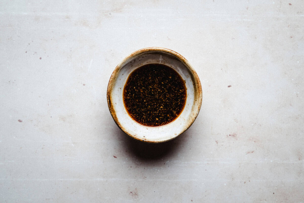 A small ceramic bowl filled with dark ponzu sauce sits on a light, textured surface.