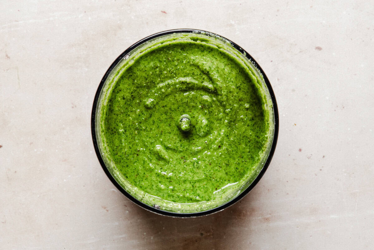 A bowl filled with smooth, vibrant green pesto, viewed from above, on a light-colored surface.