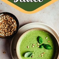 A bowl of creamy green pesto sauce garnished with basil leaves and pine nuts sits on a plate beside a small bowl filled with pine nuts. The text above reads "Creamy Pesto Sauce.