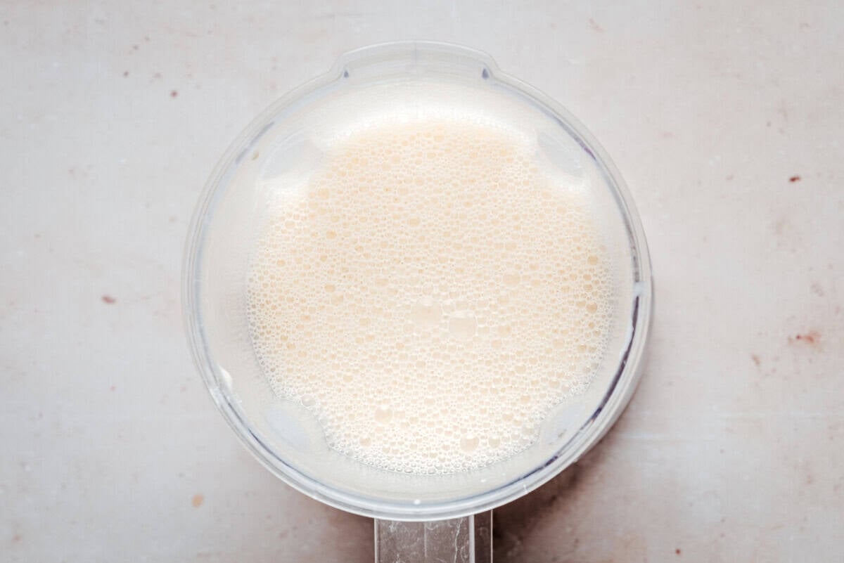 A top-down view of a blender filled with a frothy, light beige liquid sitting on a light-colored countertop.