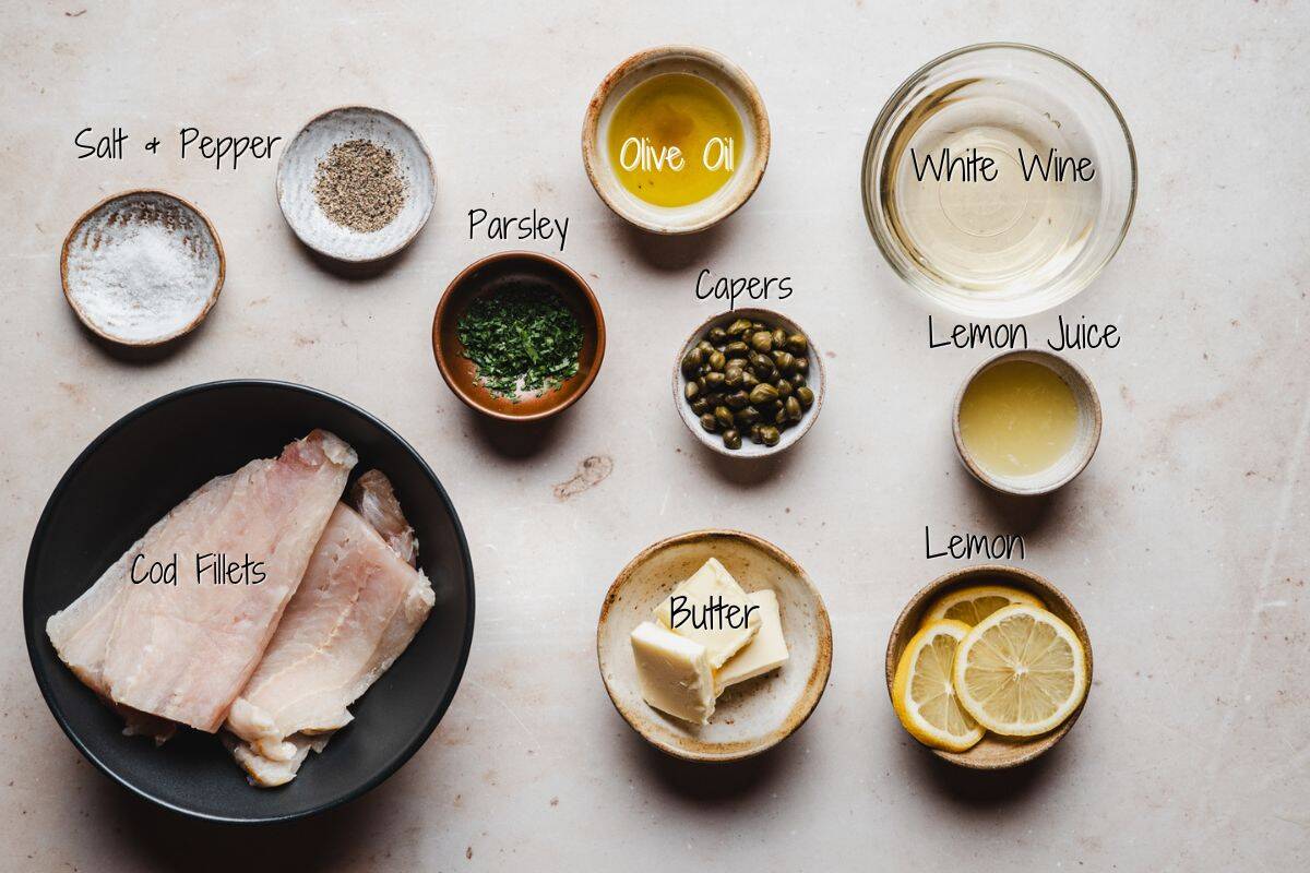 Top-down view of ingredients for Cod Piccata: cod fillets, salt, pepper, olive oil, parsley, capers, butter, white wine, lemon juice, and lemon slices arranged in bowls and plates on a light surface.