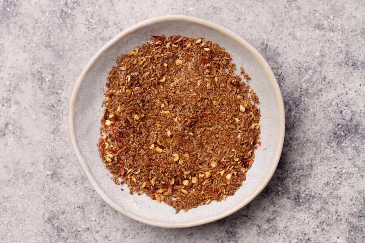 A white plate filled with spice blend containing visible red pepper flakes, set on a gray textured surface.