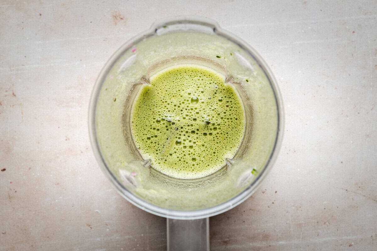 Top view of a blender containing jalapeño chile vinaigrette, likely a smoothie or juice, on a light-colored countertop.
