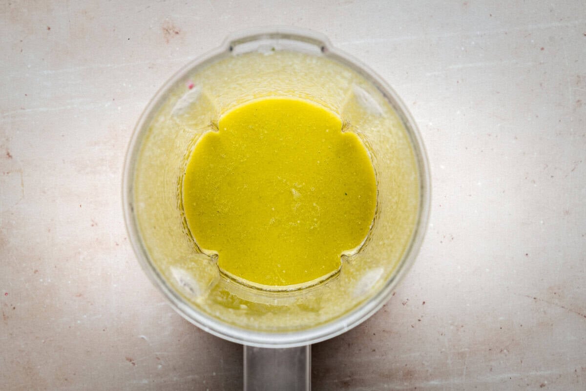 A top-down view of a blender containing a smooth, yellow-green liquid mixture, set on a light, speckled countertop.