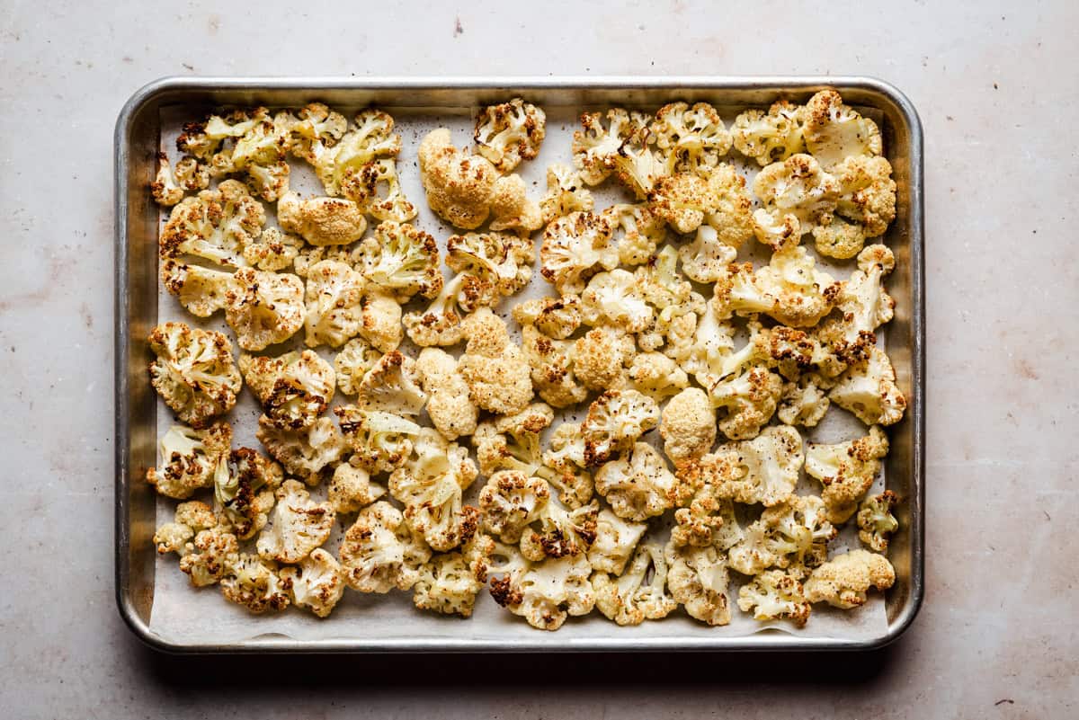 A baking sheet lined with parchment paper holds roasted cauliflower florets, golden brown and slightly crisp around the edges.